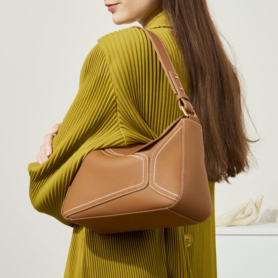 Woman wearing a brown handbag over her shoulder against a neutral background