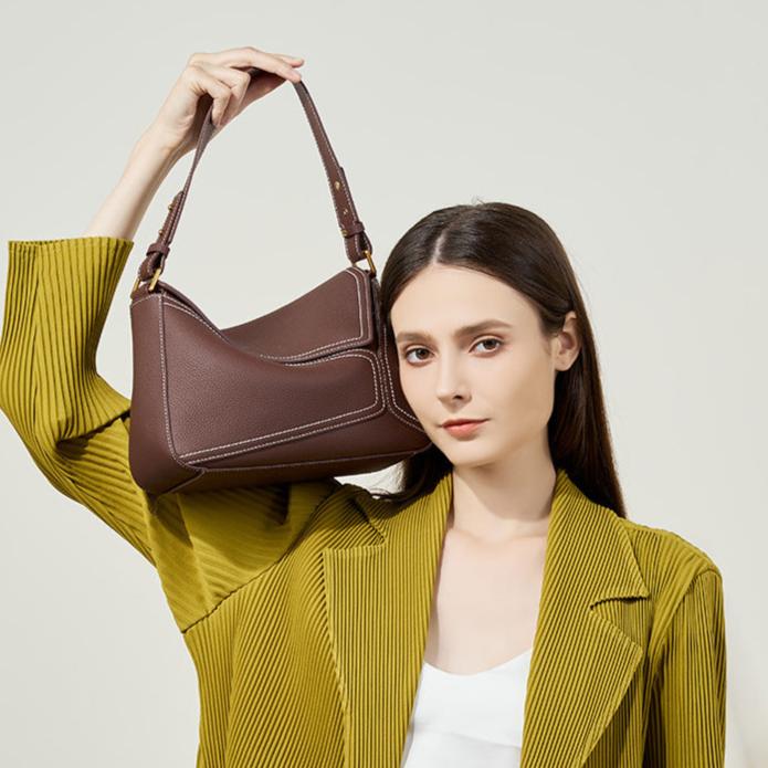 Woman holding a brown leather handbag against a plain background