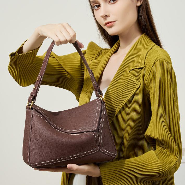 Woman holding a brown handbag against a plain background