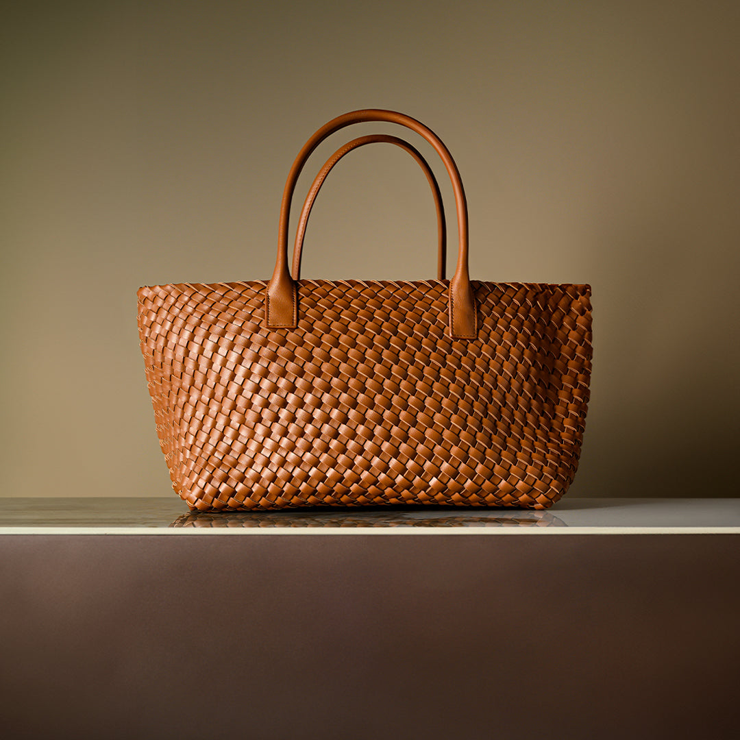 Brown woven handbag on a reflective surface with a gradient background