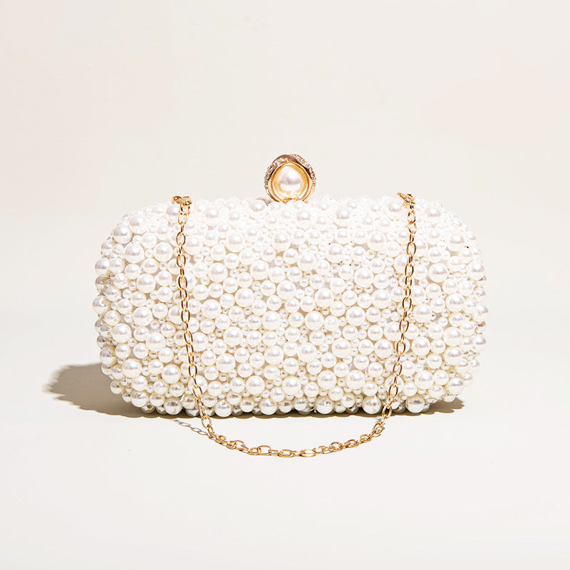 Pearl-handled clutch bag with gold chain on a light beige background
