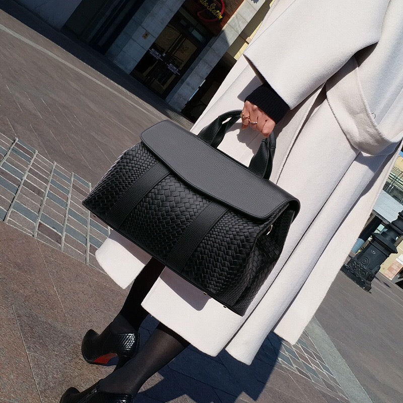 Person holding a black woven handbag on a city street