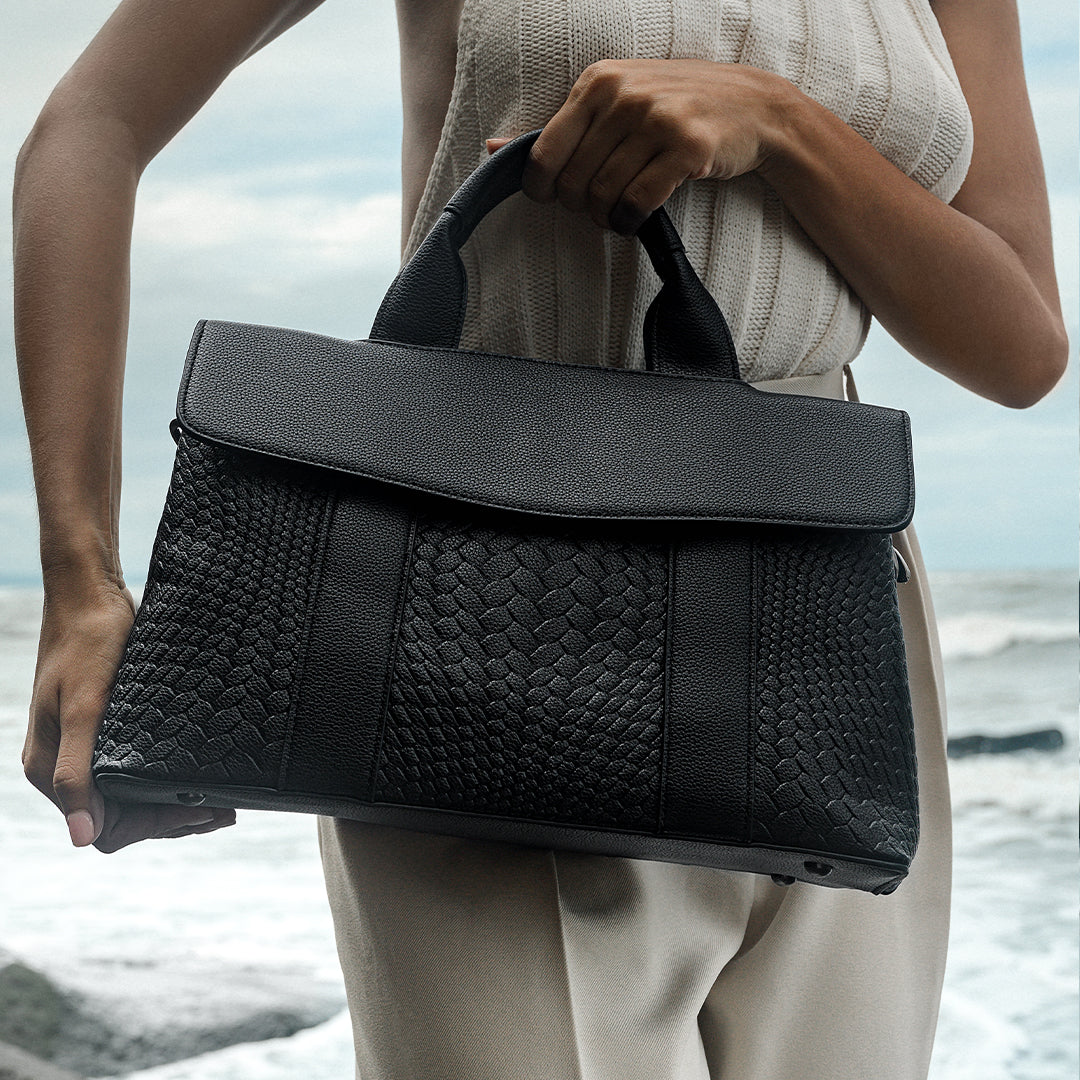 Person holding a black woven handbag by the beach