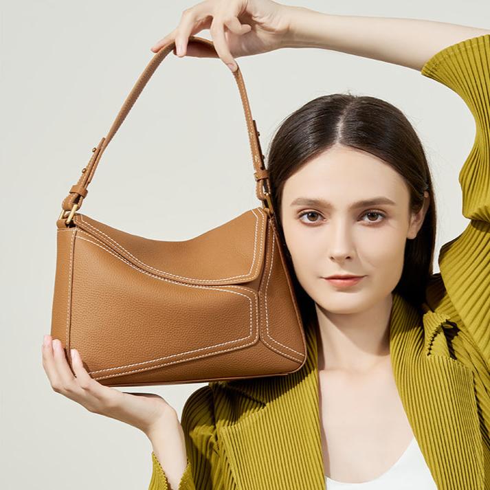 Woman holding a brown handbag against a plain background