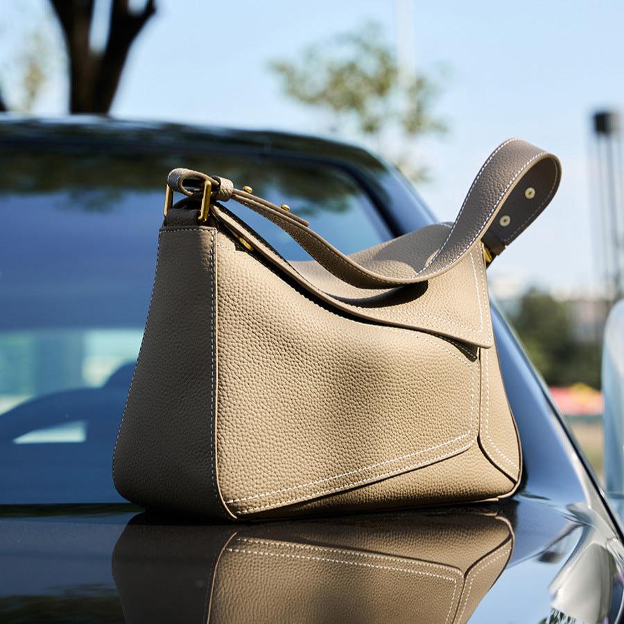 Beige handbag on a car hood with a blurred outdoor background