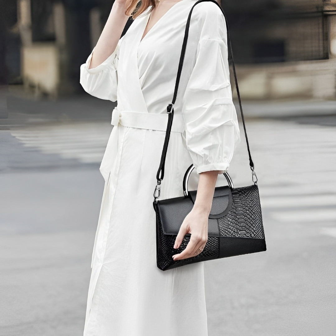 Person holding Ava black handbag with a textured pattern on a blurred street background