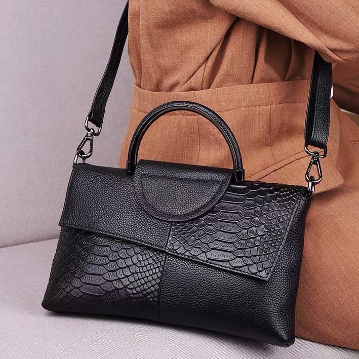 Black textured handbag with a handle and strap, placed against a brown fabric background.