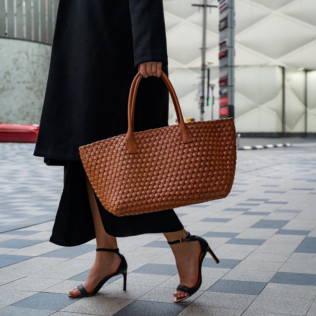 Person holding a brown woven handbag on a city street.