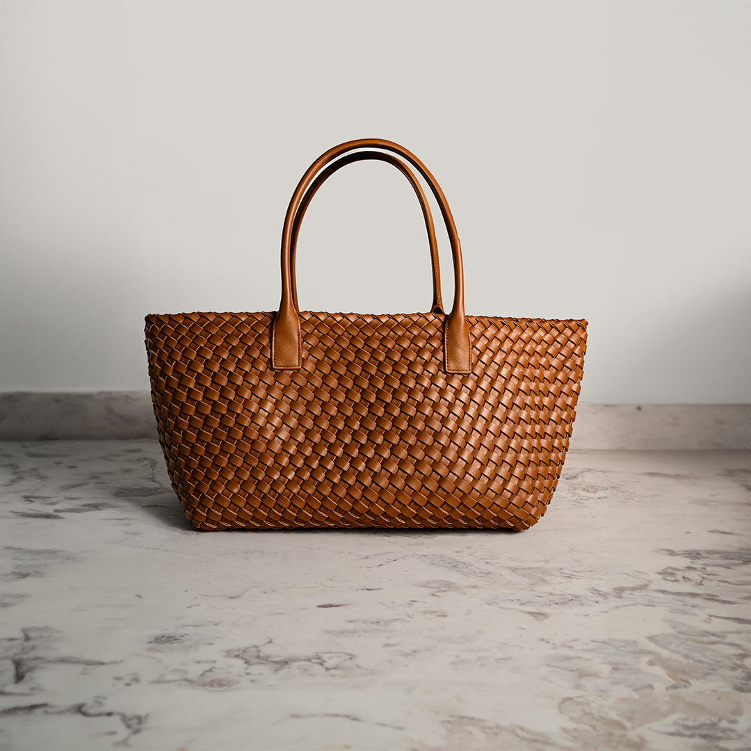 Brown woven handbag on a marble surface with a neutral background