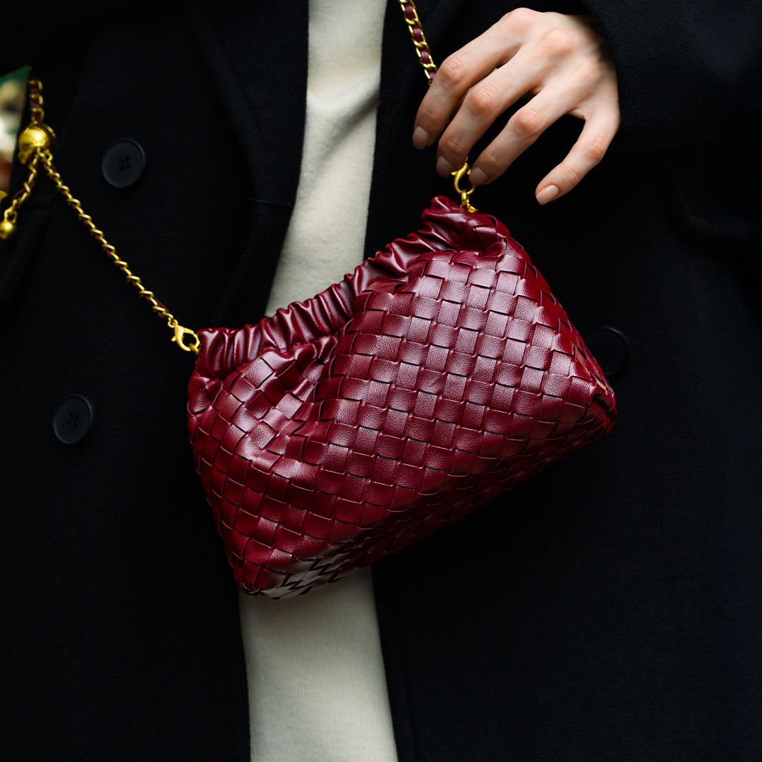 Red woven handbag with gold chain strap held by a person wearing a black coat.