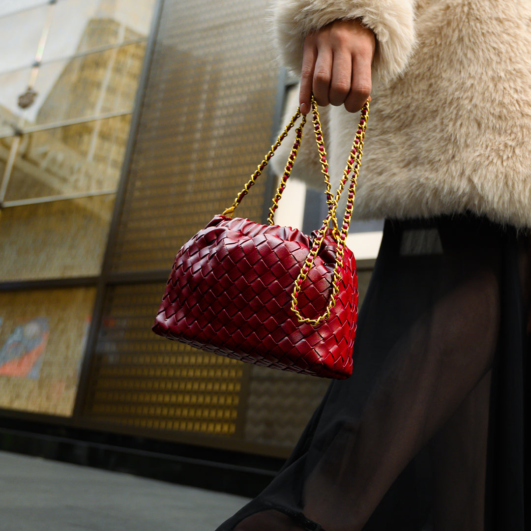 Red woven handbag with gold chain held by a person wearing a fur coat.