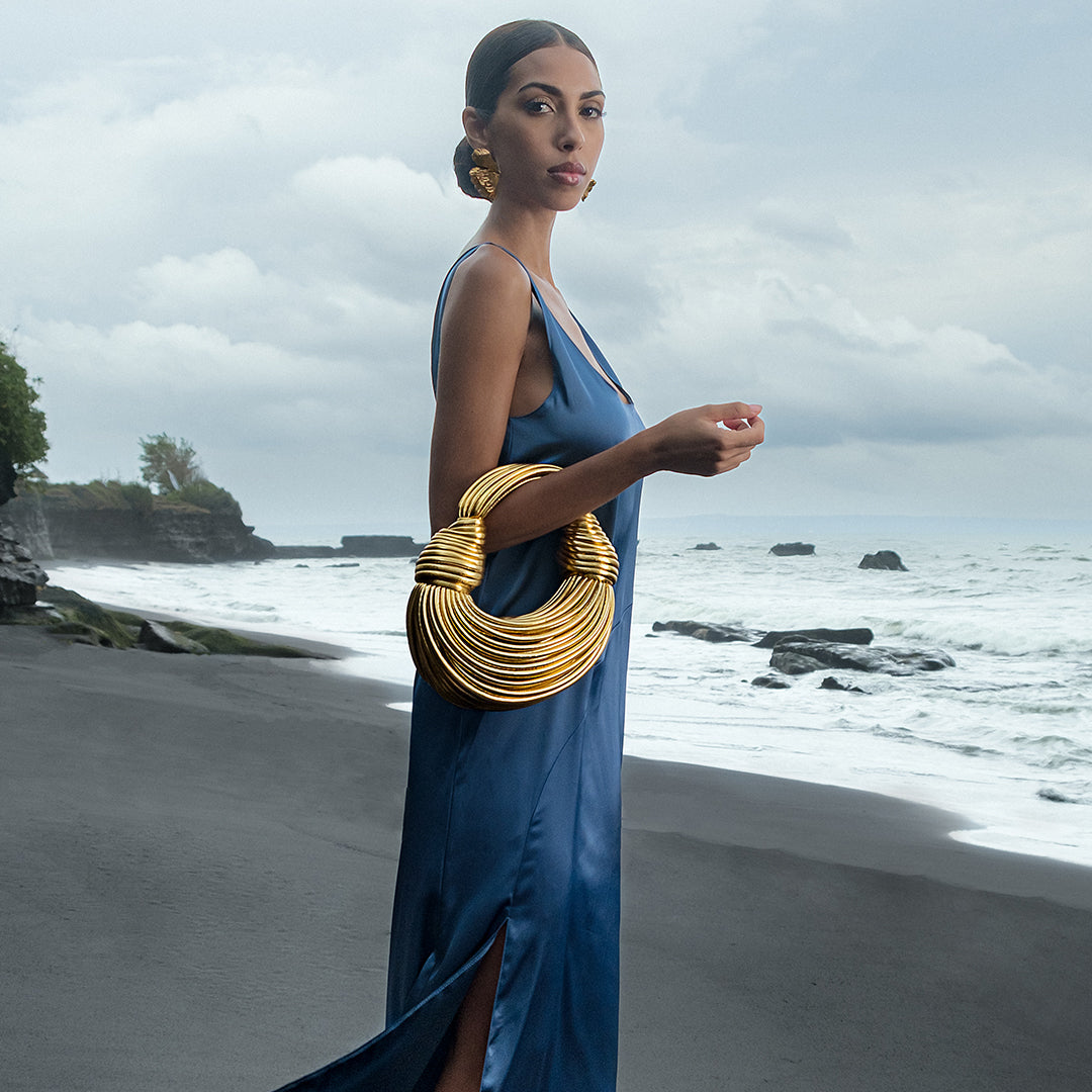Woman in a blue dress with a gold handbag on a beach