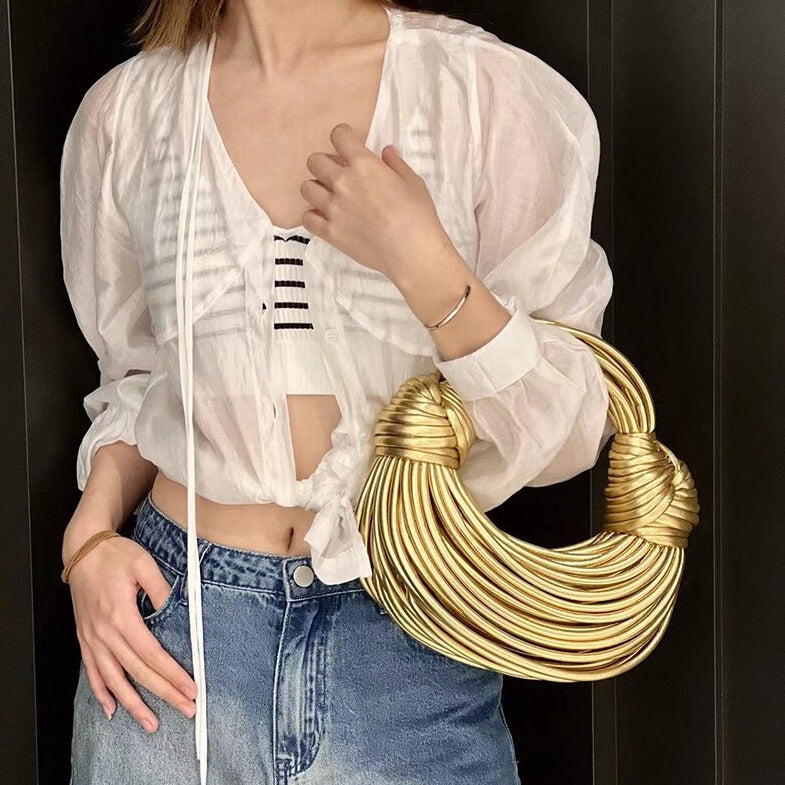 Person wearing a white blouse and blue jeans holding a gold handbag against a black background