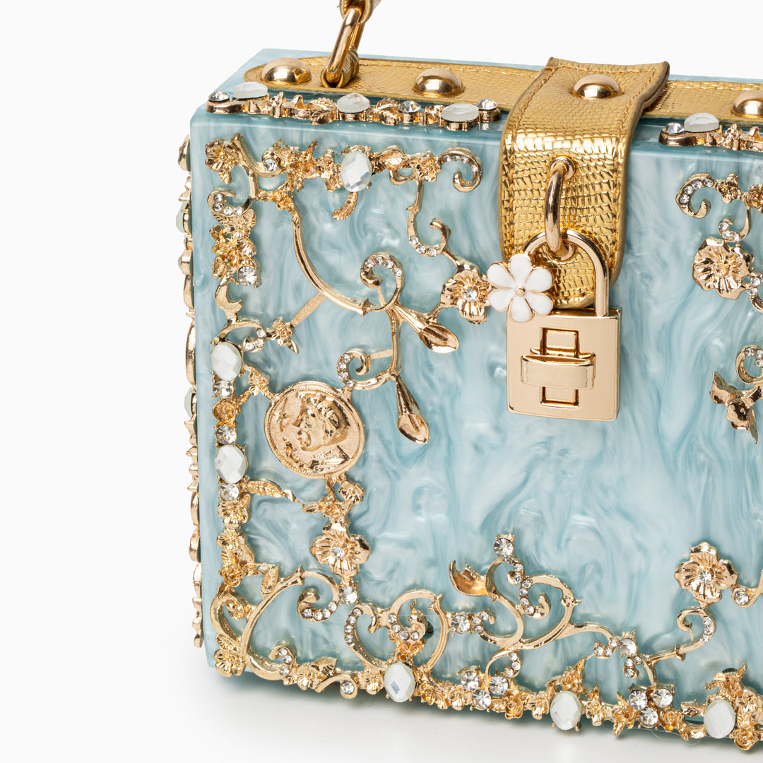 Handbag with gold embellishments and a lock on a light blue background
