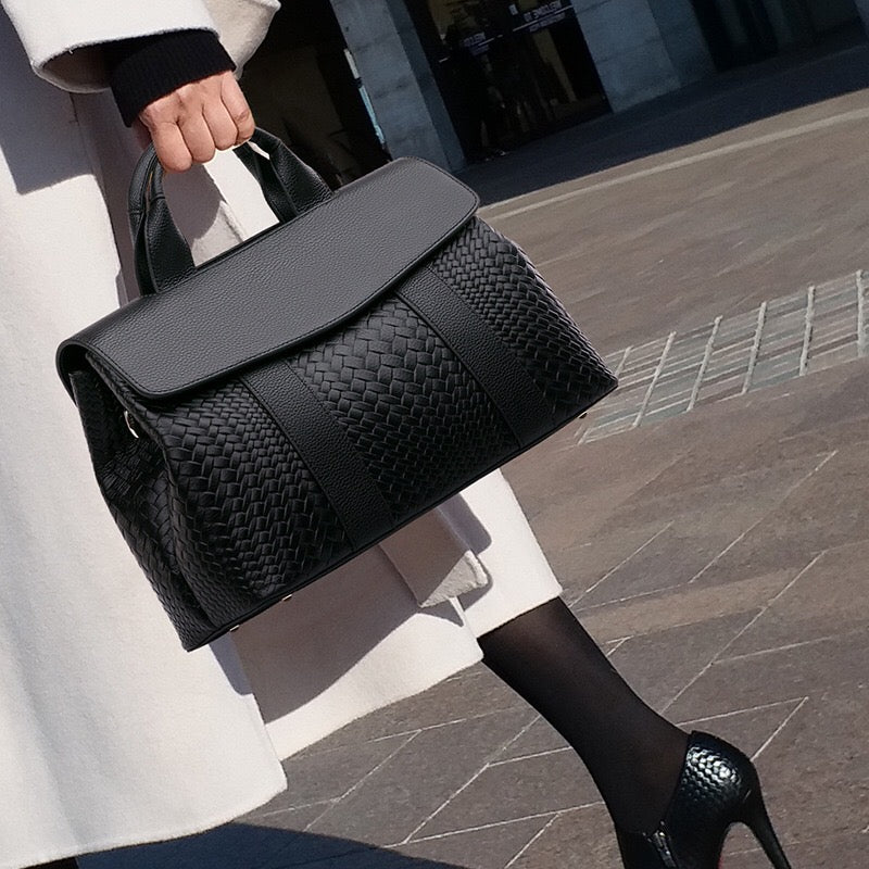 Person holding a black woven handbag on a city street